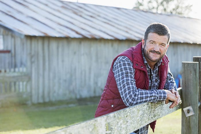 Man outside barn leaning on wooden fence