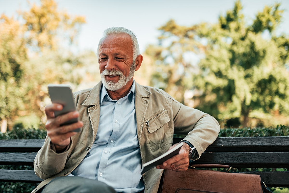 Senior man reading online news on smartphone outdoors.