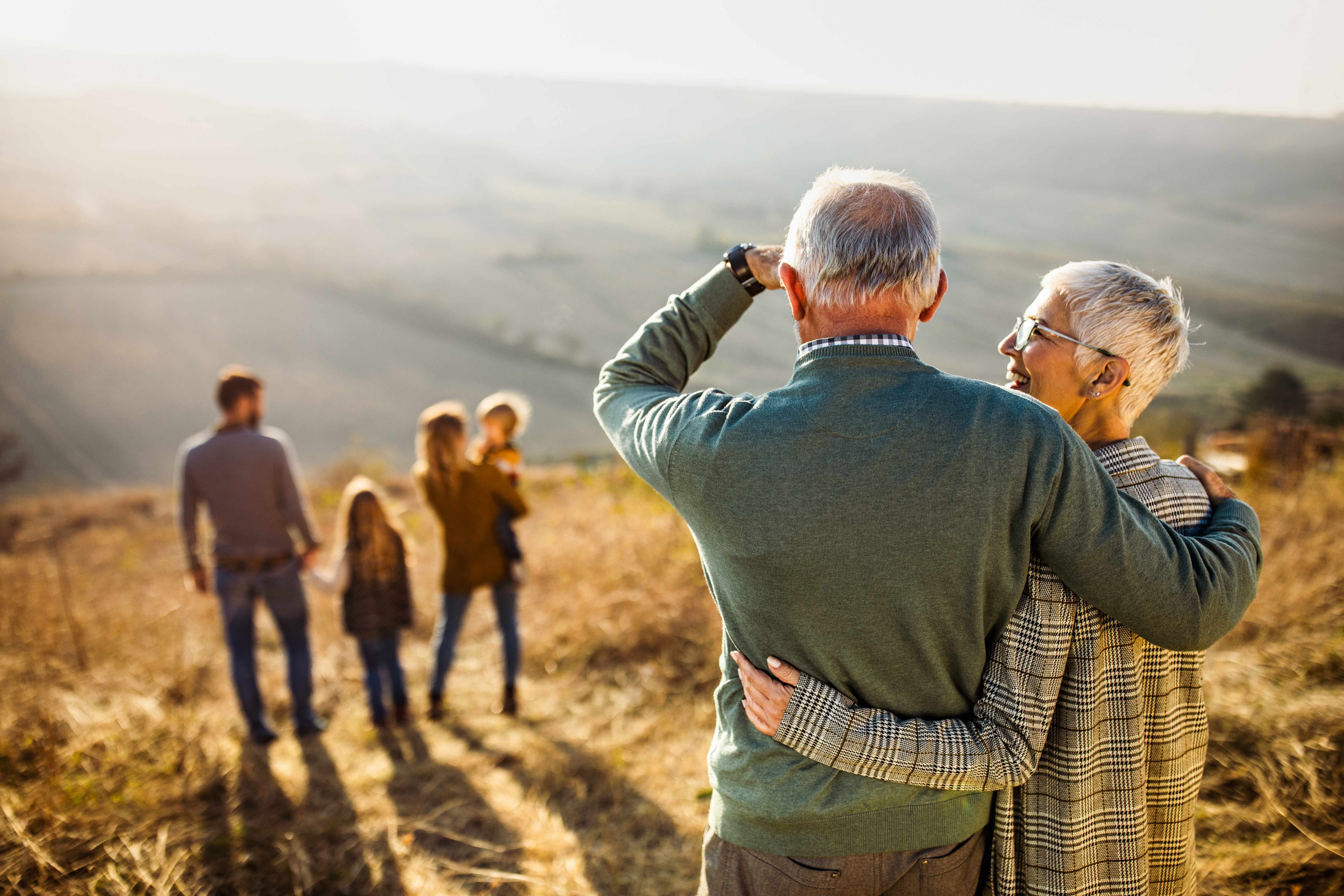 Grandparents lovingly looking over their children and grandchildren off in the distance.