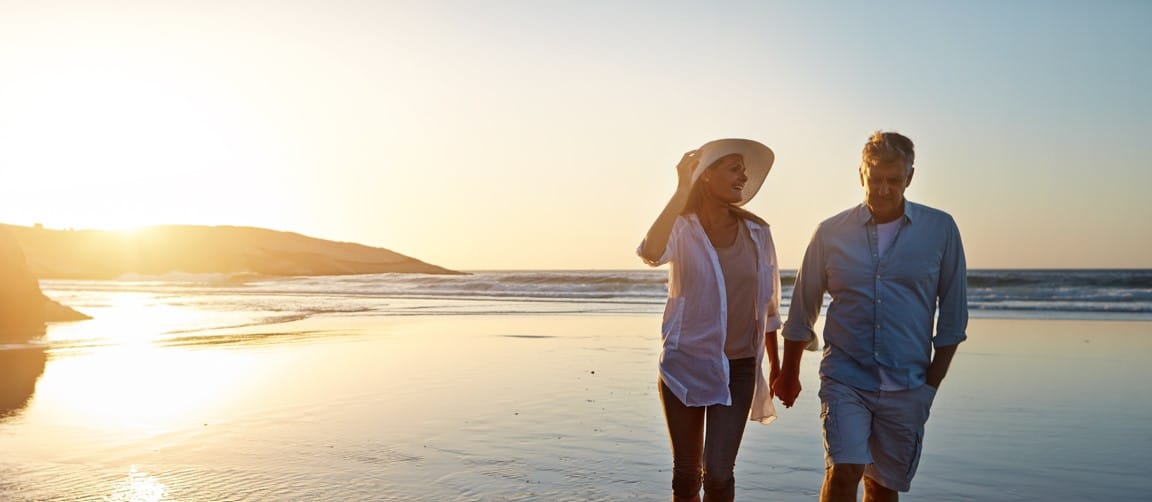 Couple walking on beach with sunset in back.