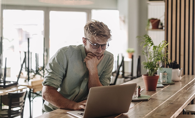 Young man working in his start-up cafe, using laptop