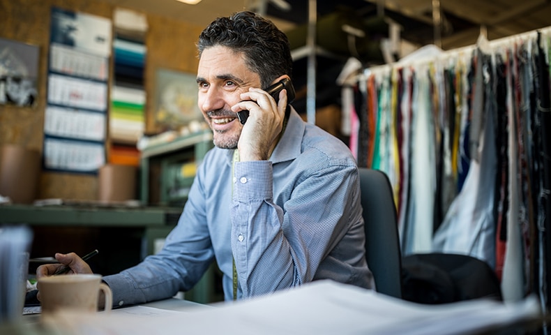 Happy mature businessman sitting at his desk talking on cordless phone. Fashion shop owner having telephonic conversation with client.