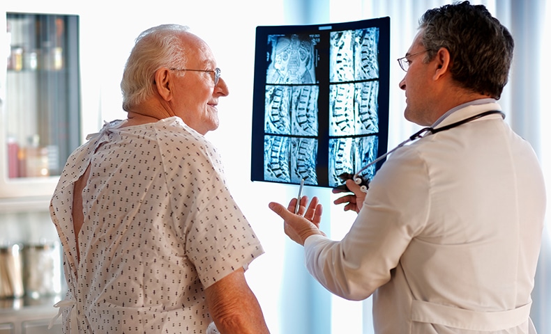 Doctor talking to senior male patient while holding up MRI