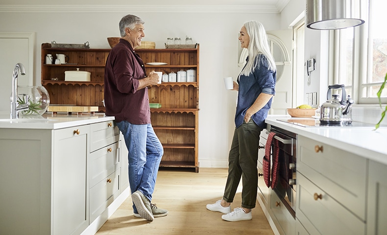 Mature man and woman having coffee. Couple talking while standing in kitchen. They are spending leisure time at home.