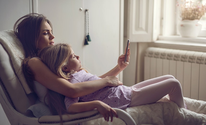 Mother and daughter in rocking chair using mobile phone.